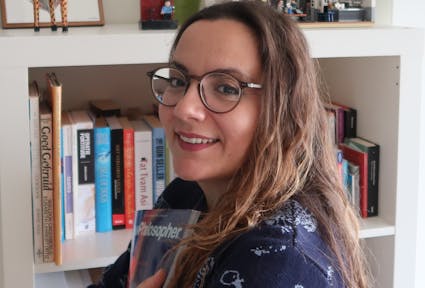 Paola Chiara Masuzzo, standing in fron of a book shelf, holding an issue of "Philosopher" magazine"