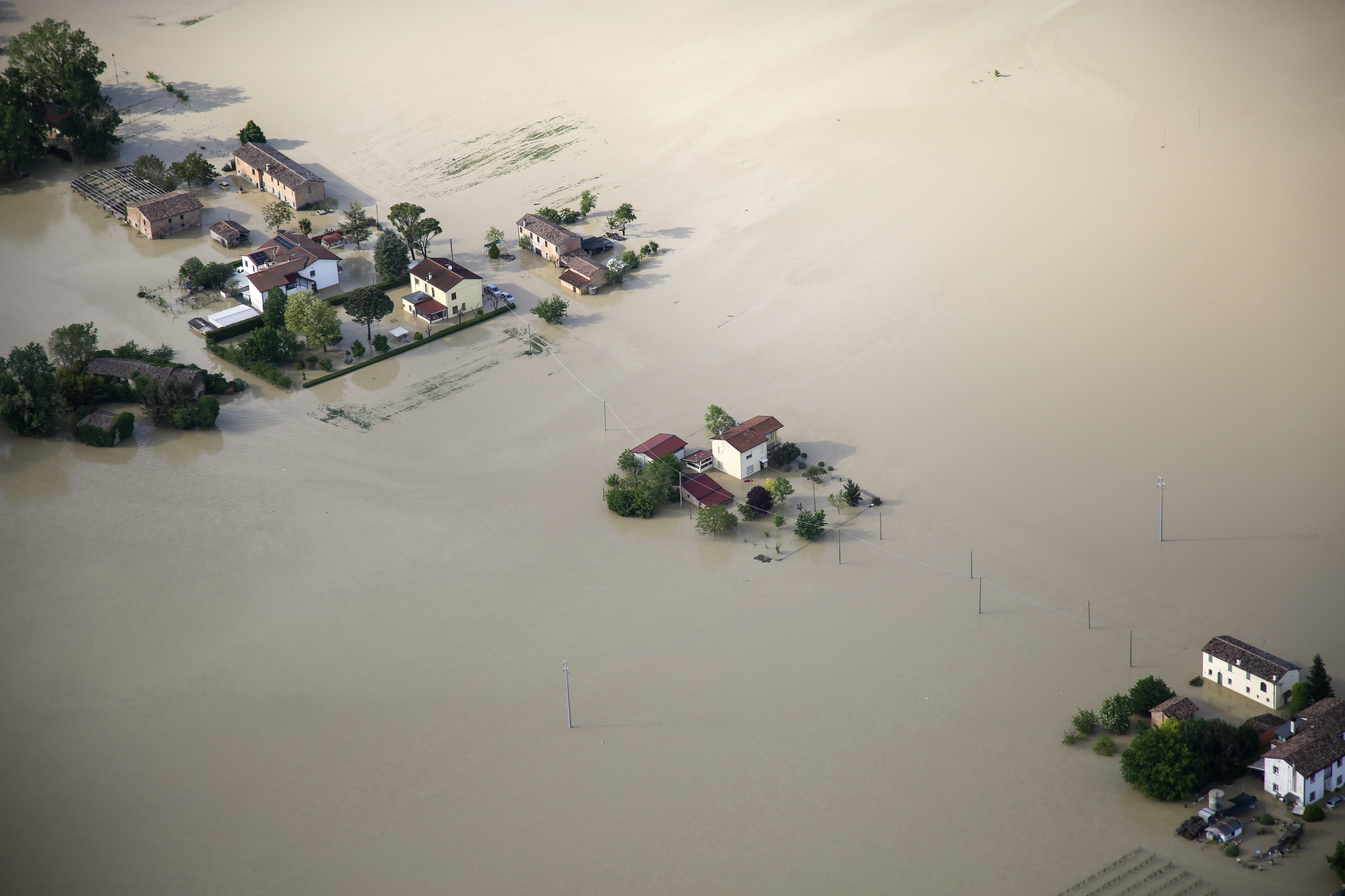 A few houses and trees sticking out from brown floodwater, in Emilia Romagna. Bird's eye view.