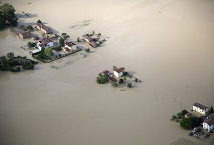 A few houses and trees sticking out from brown floodwater, in Emilia Romagna. Bird's eye view.