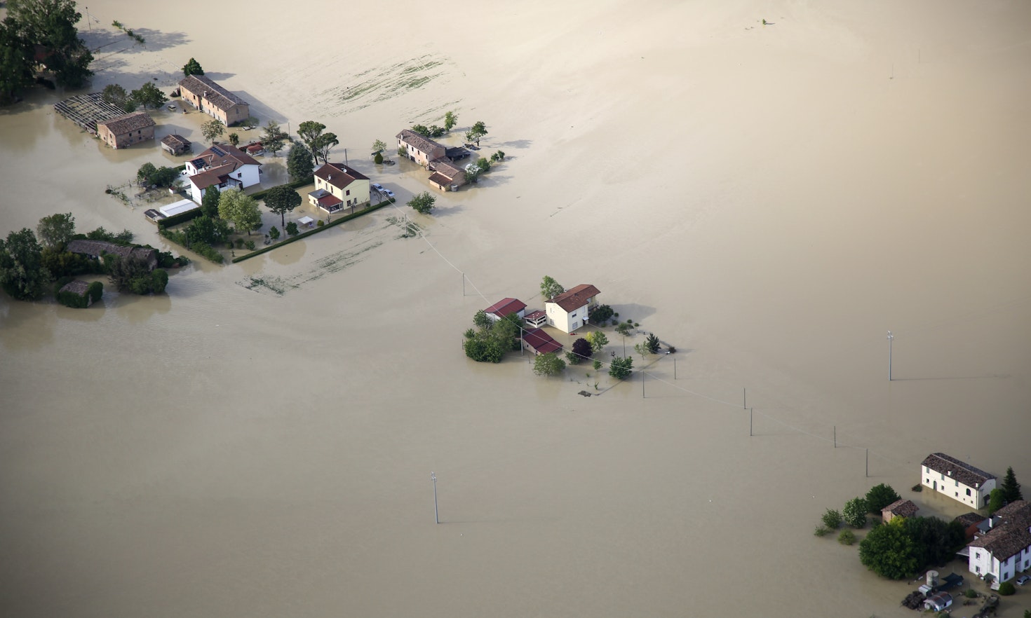 A few houses and trees sticking out from brown floodwater, in Emilia Romagna. Bird's eye view.