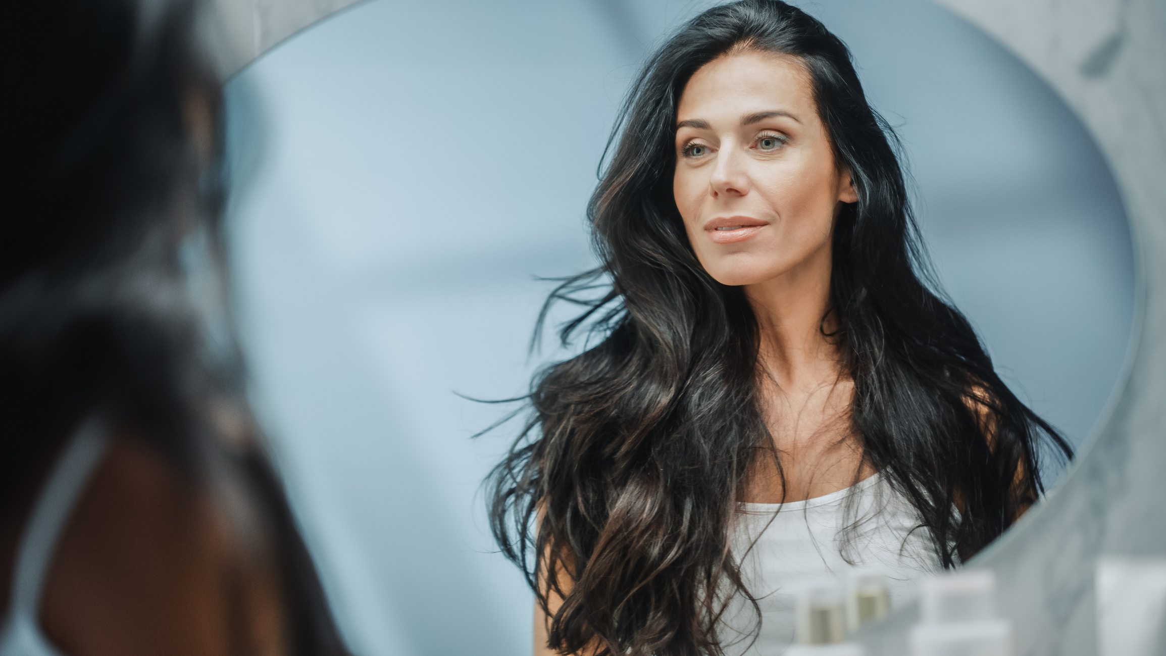 Middle-aged woman with dark hair looking into a mirror