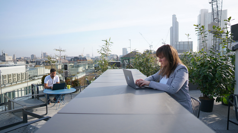 Two people work on the rooftop, surrounded by plants and with a direct view across London
