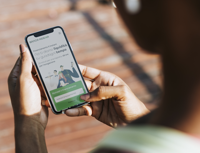 A hand holding a smartphone that shows Banca AideXa's Corporate Website home page