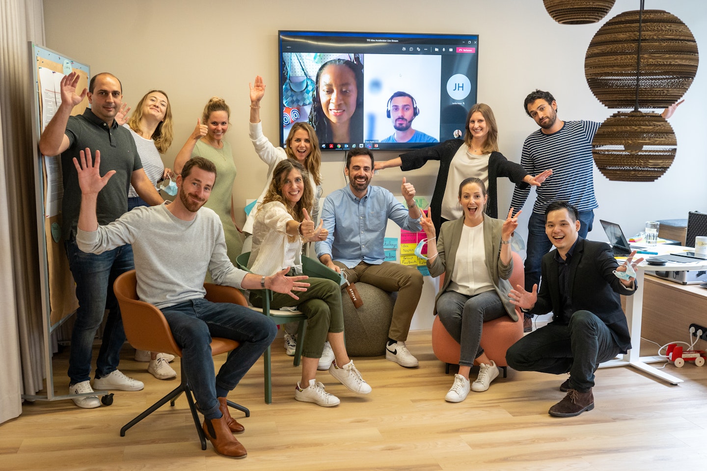 13 member team photo, 11 people in Tangity Munich Studio, 3 connected via Teams on television