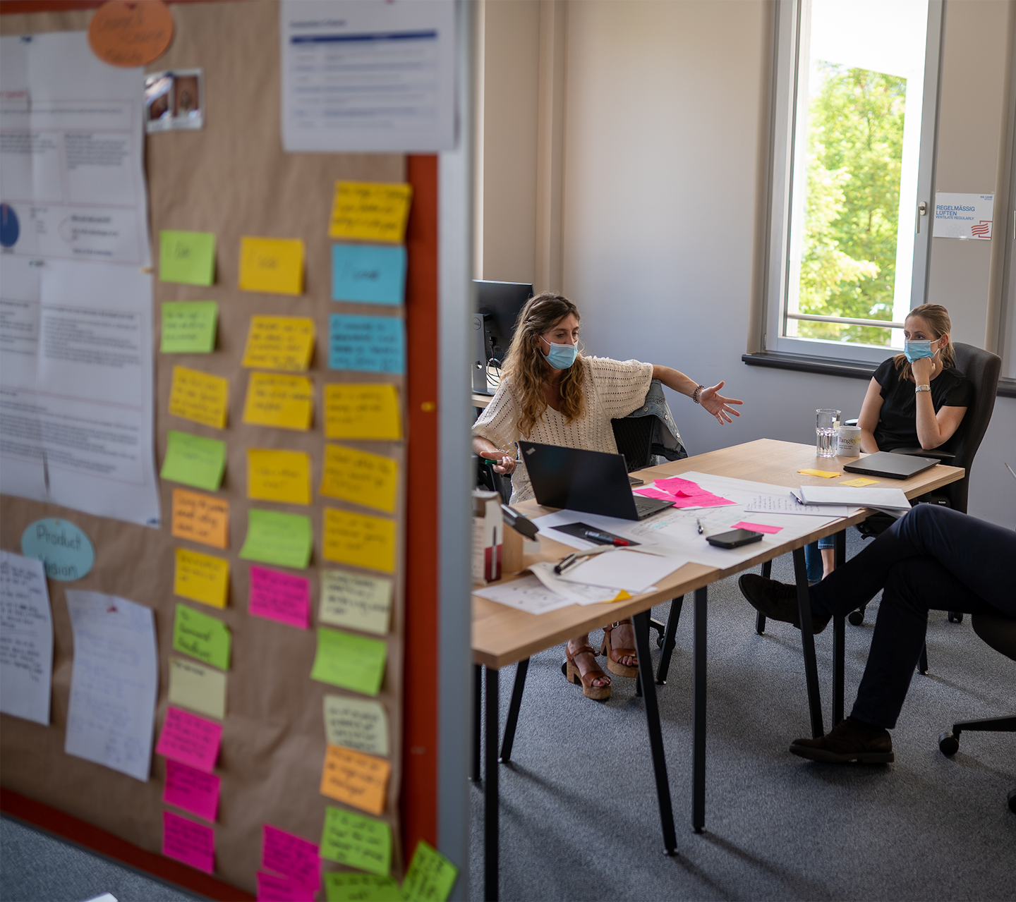 Two women and one man from TFS Innovation Team holding a meeting sitting at a table behind a whiteboard