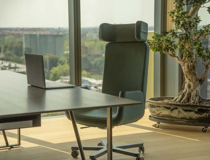 Green Silente chair in the office with a laptop on the table in the foreground and a tree and big windows in the background