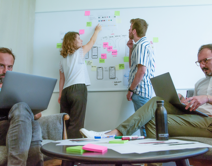 Four designers during a work session, two sitting at their laptops, two working at a white board