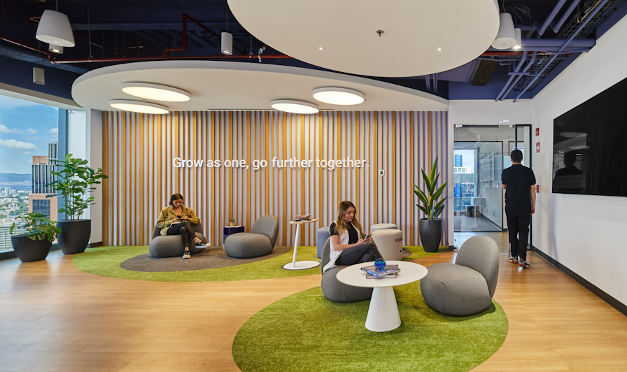 Three people in open space with writing on wall saying Grow as one, go further together