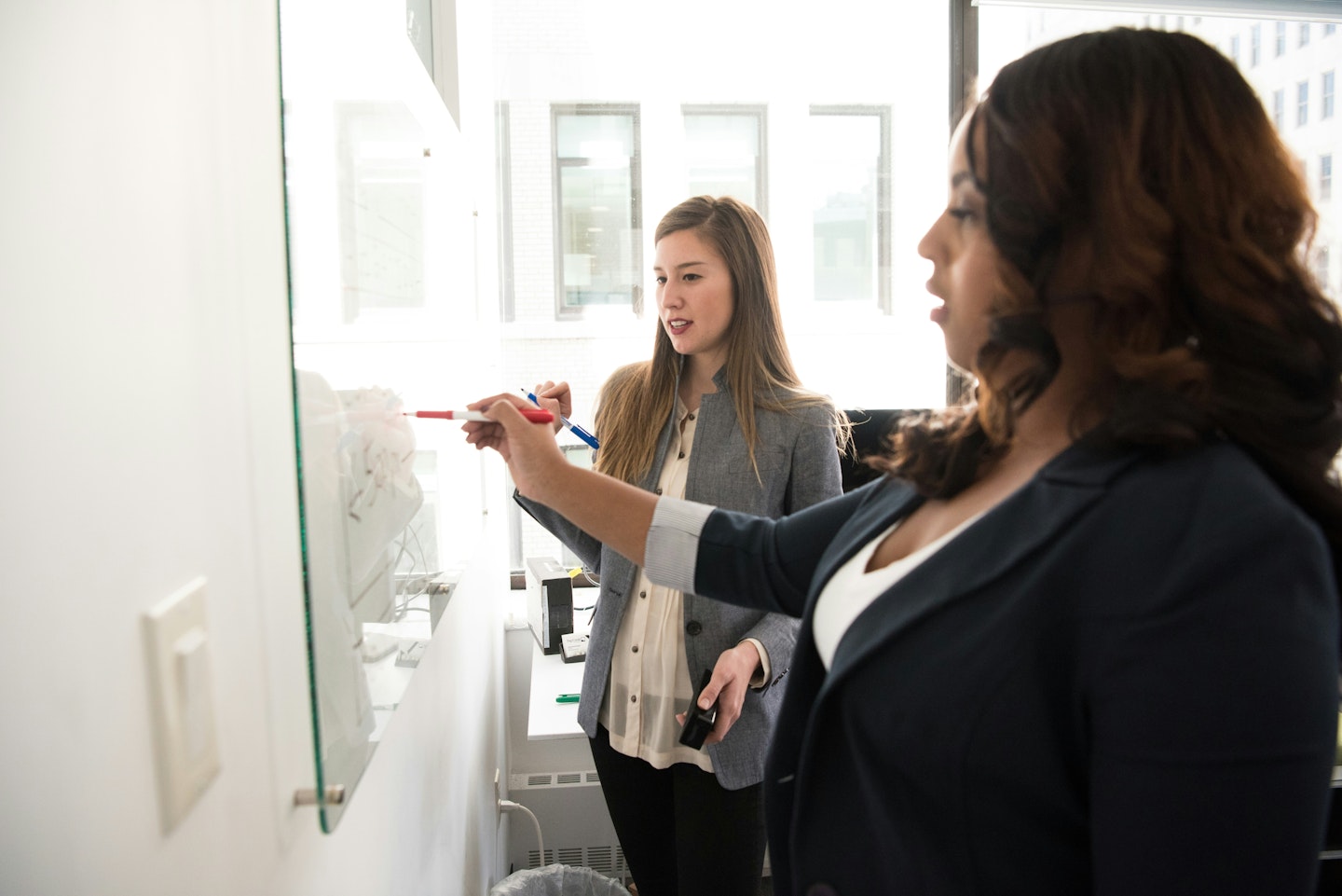 Two people writing on glass board