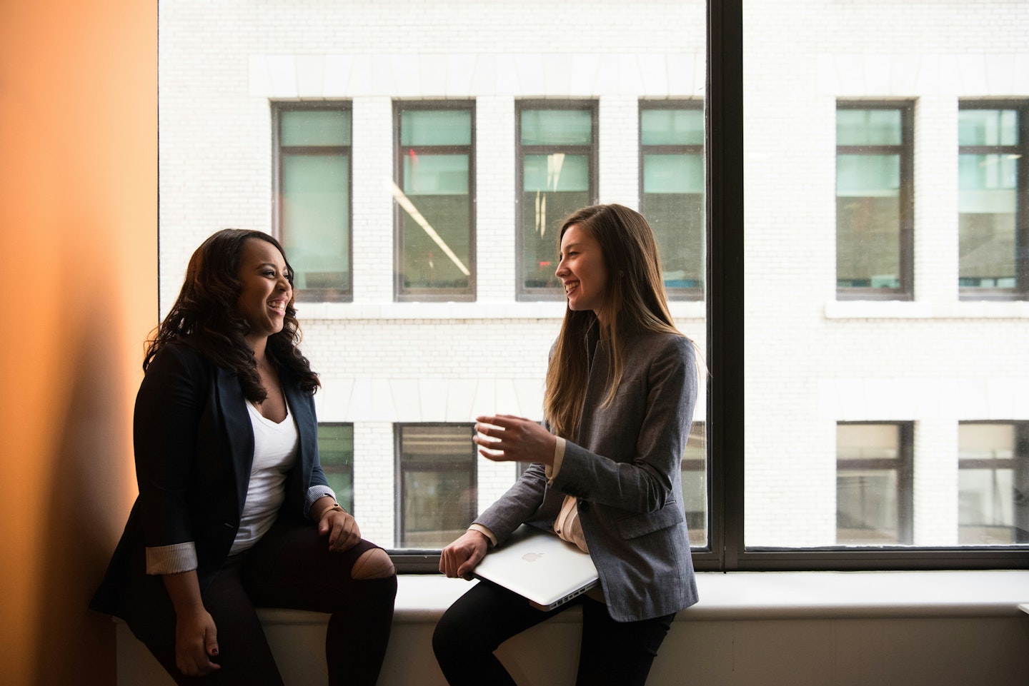 Colleagues chatting and smiling sitting on the windowsill