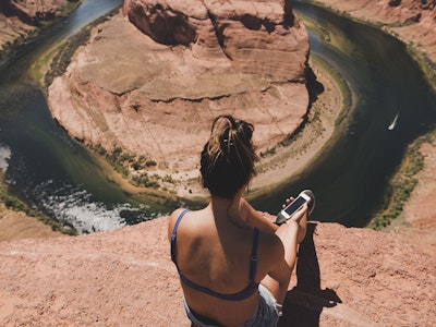 Woman sitting on cliff looking at canyon river