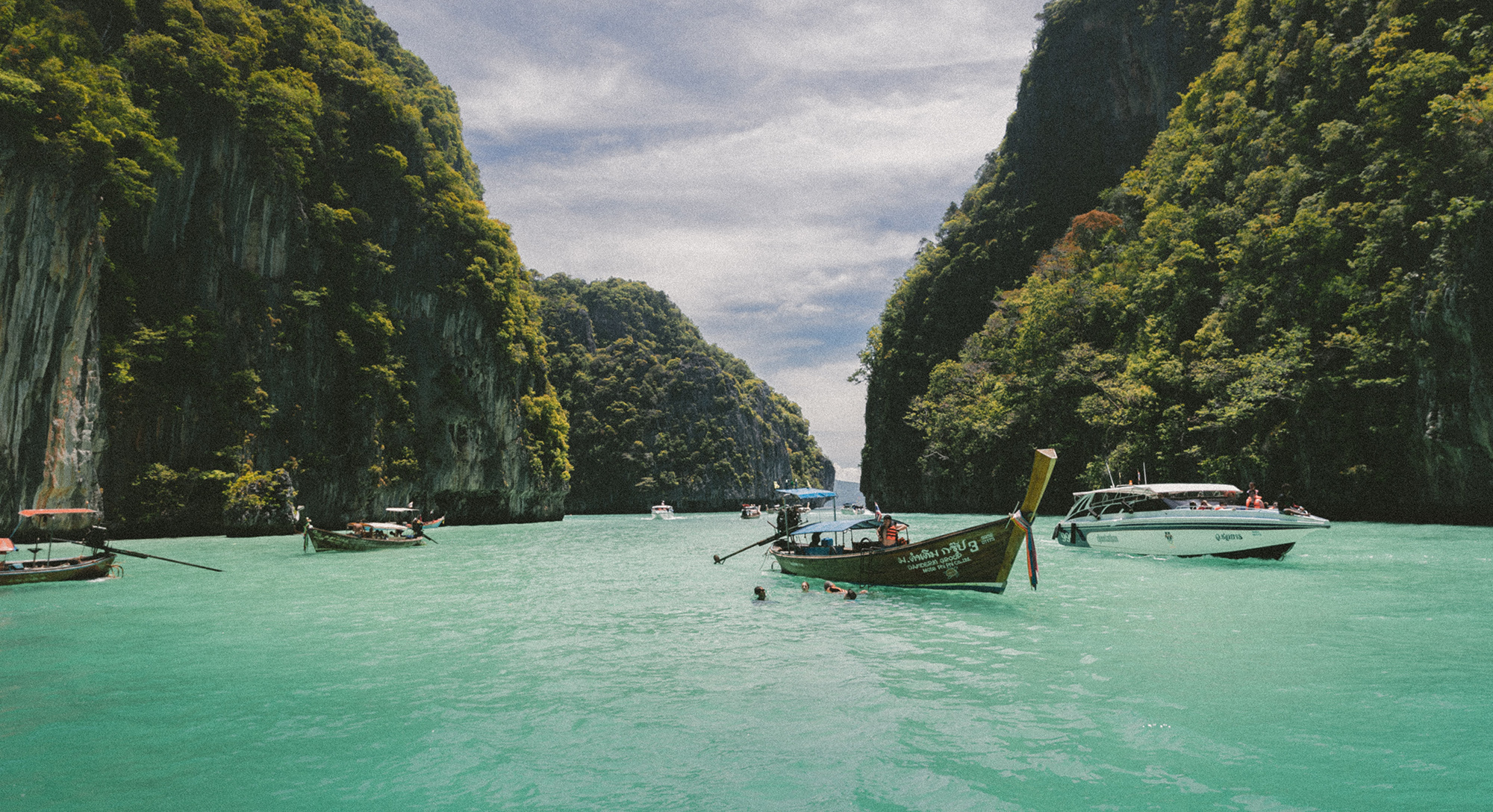 Small boats in river flanked by green covered mountains