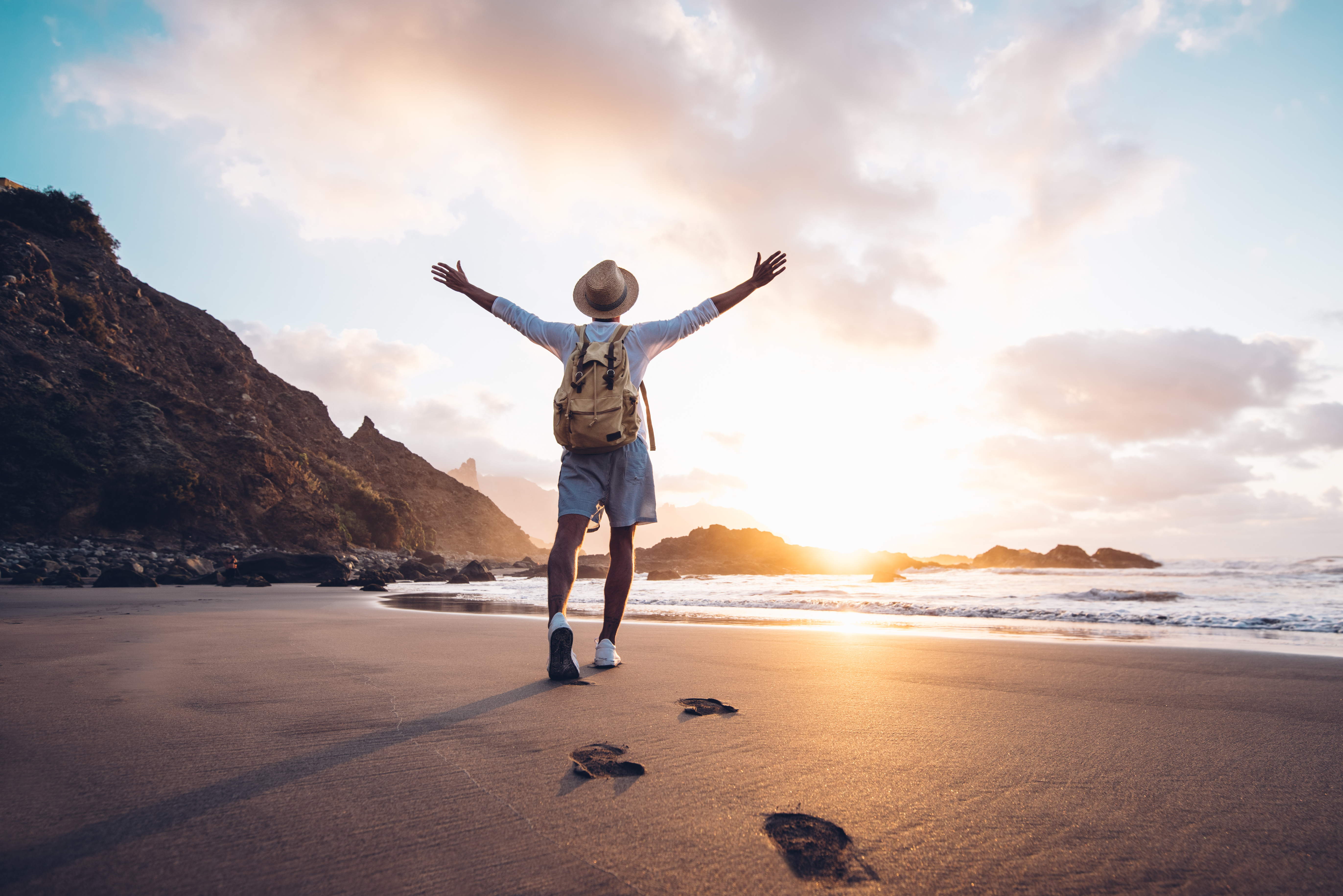 Young man walking on beach with outstretched arms