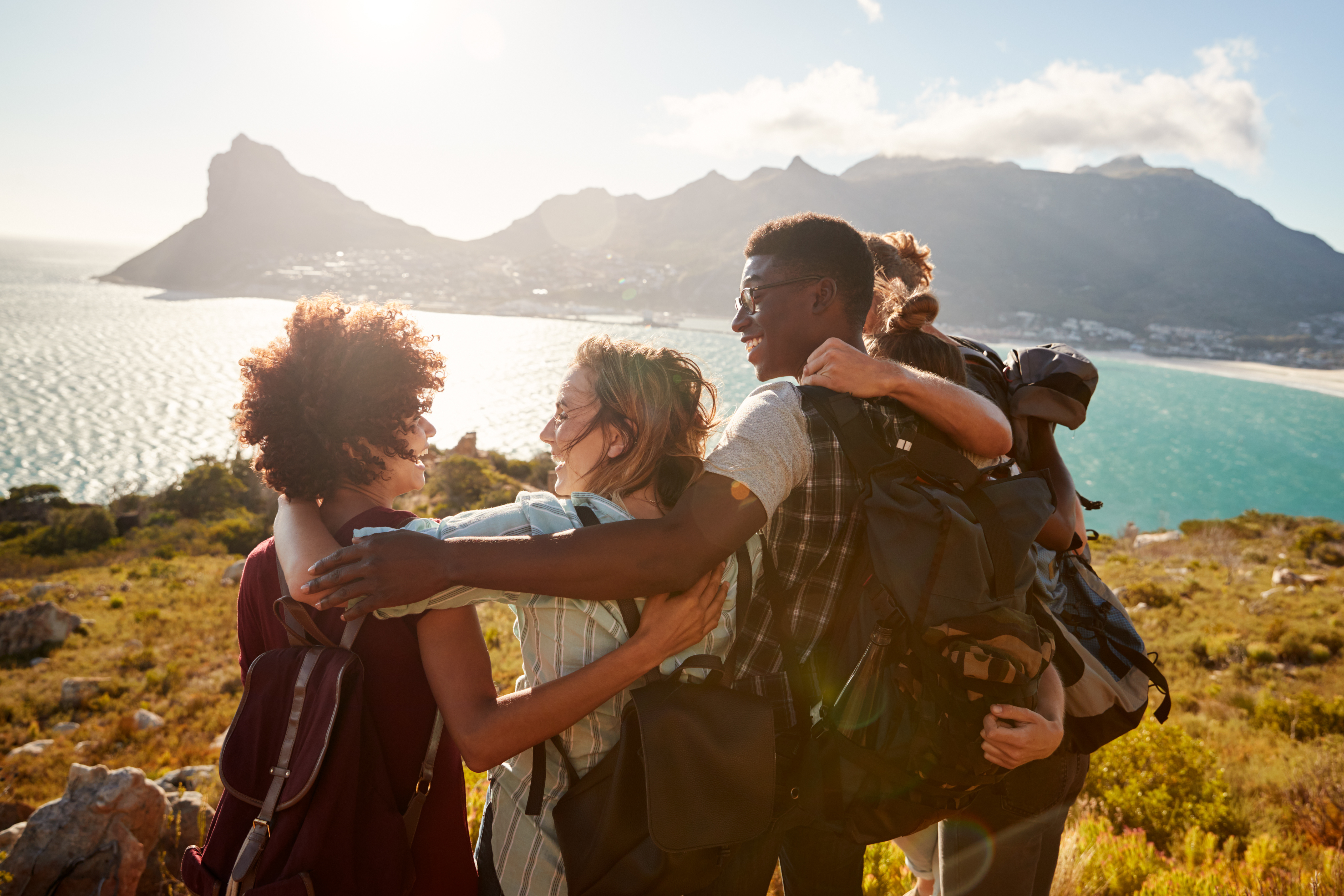 Four friends embracing on cliff overlooking bay