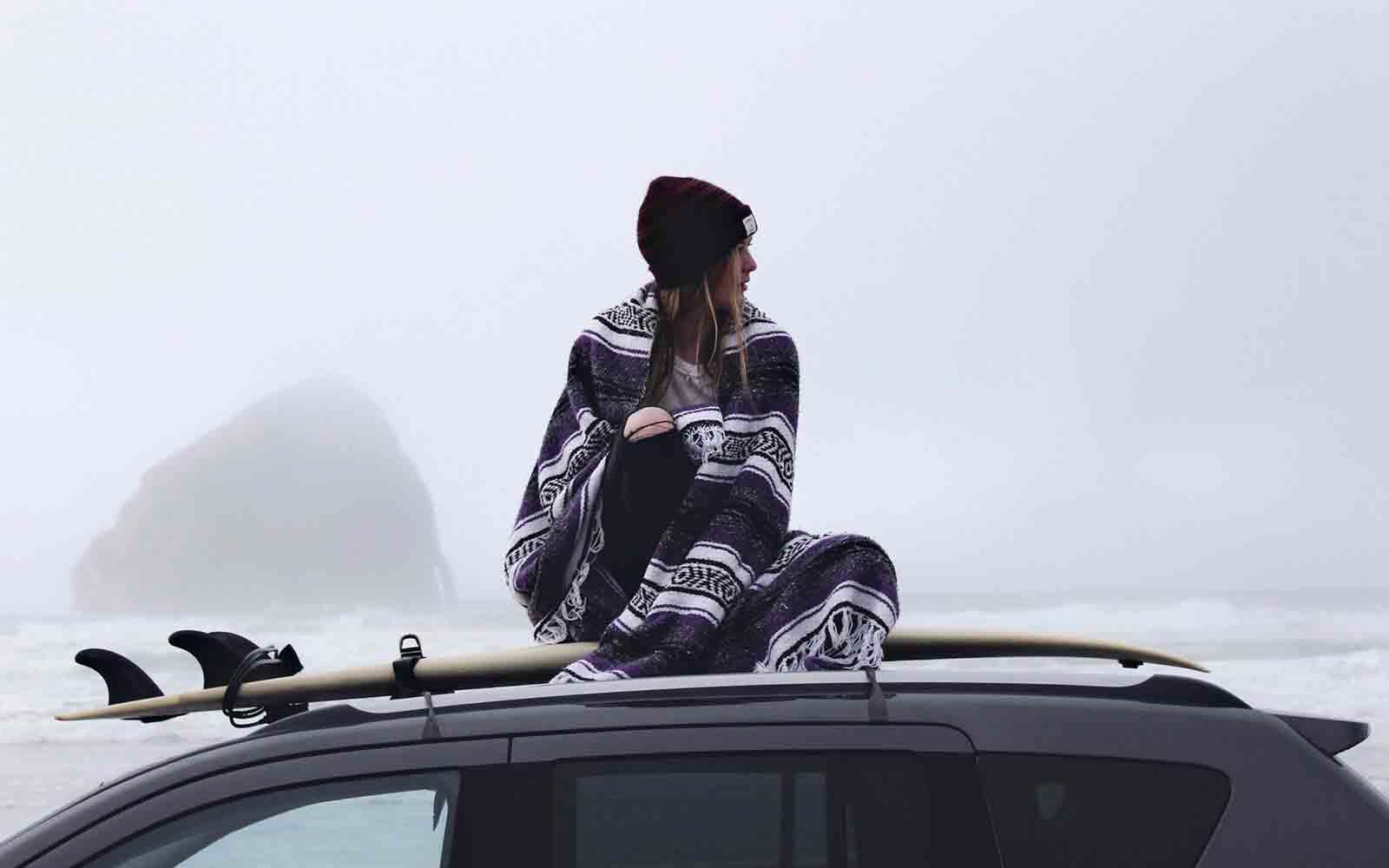 Woman with surfboard sitting on top of car