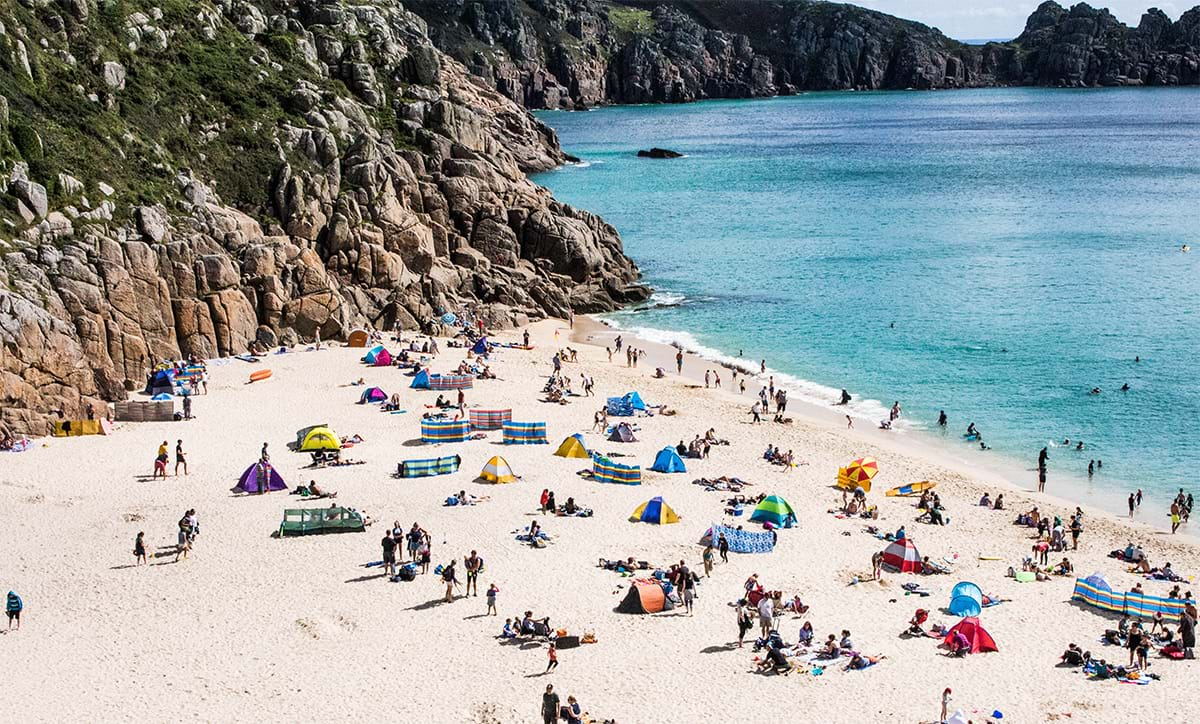 Beach full of people and surrounded by rocky cliffs