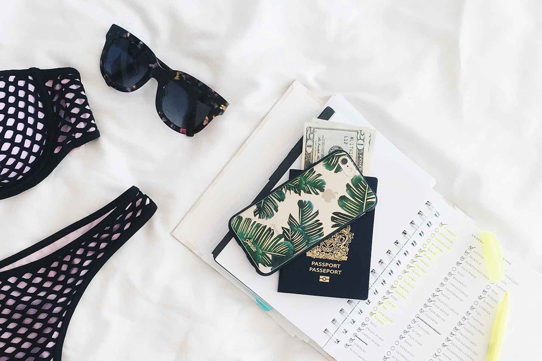 Photo of swimsuit, sunglasses, passport, cash, phone and planner