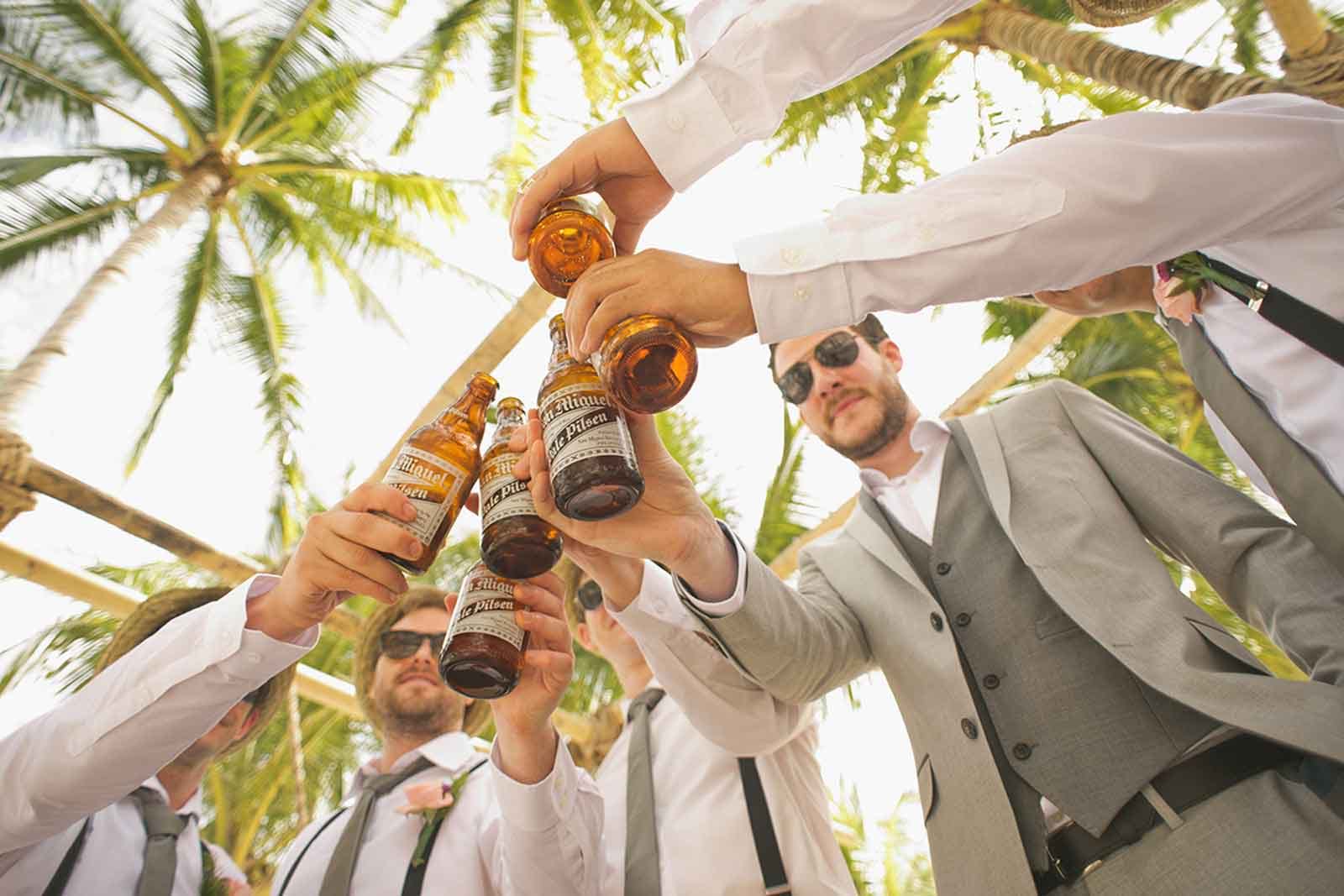 Men in suits toasting beer bottles near palm trees