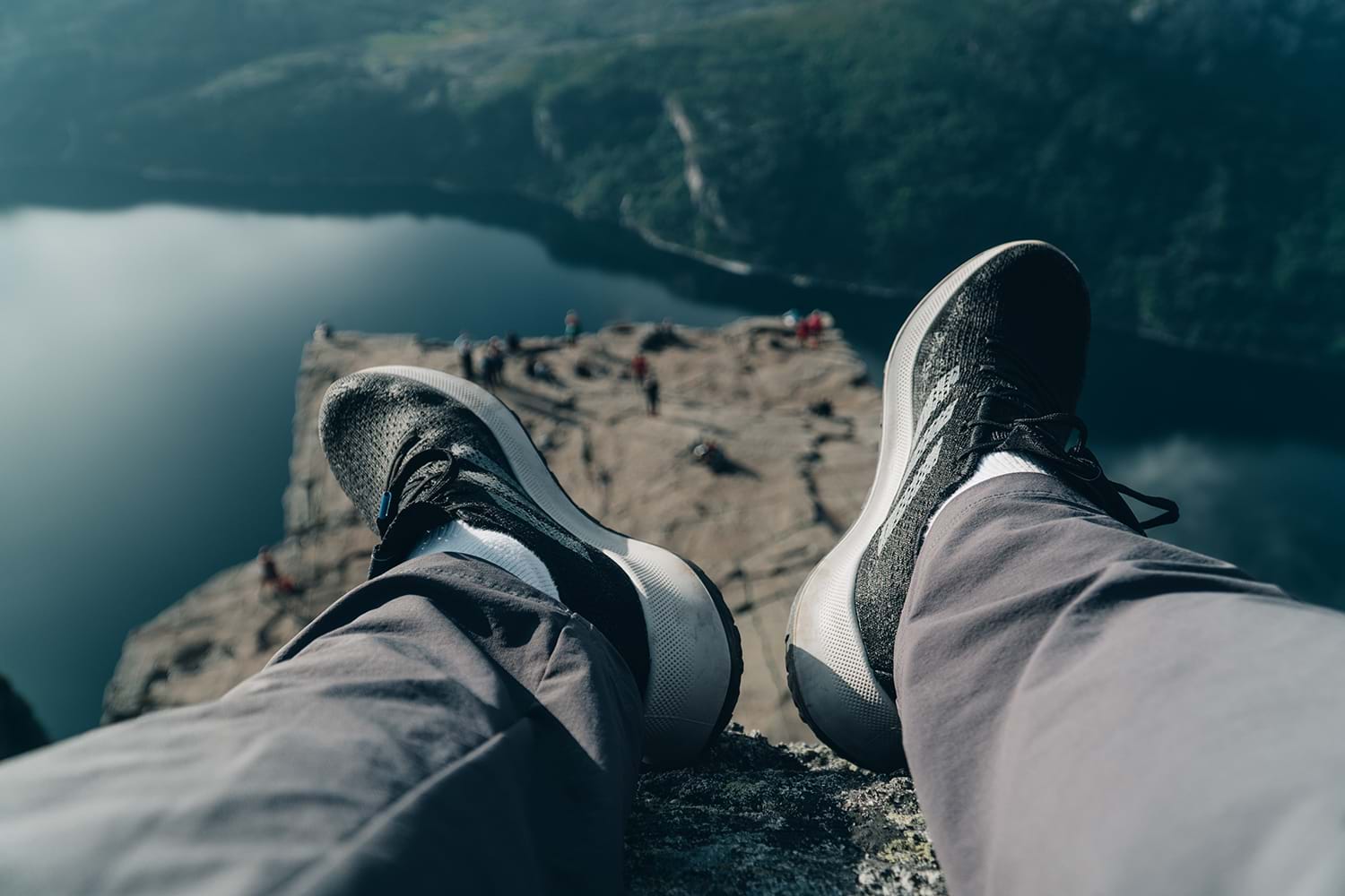 A person's feet on a cliff edge over a lake