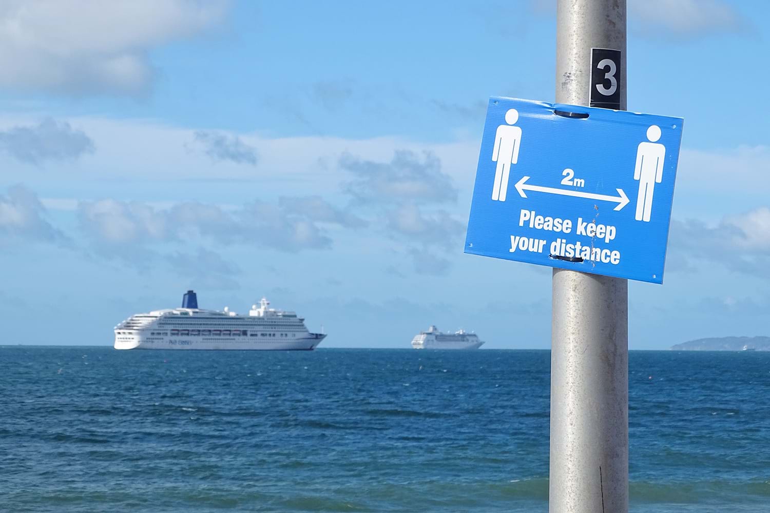 Keep distance sign with distant cruise ships at sea in background