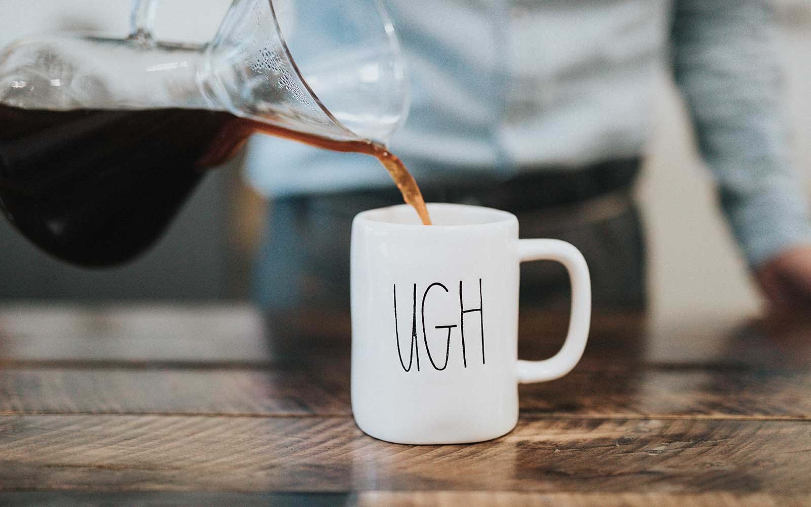 Pouring coffee into mug that says "ugh"