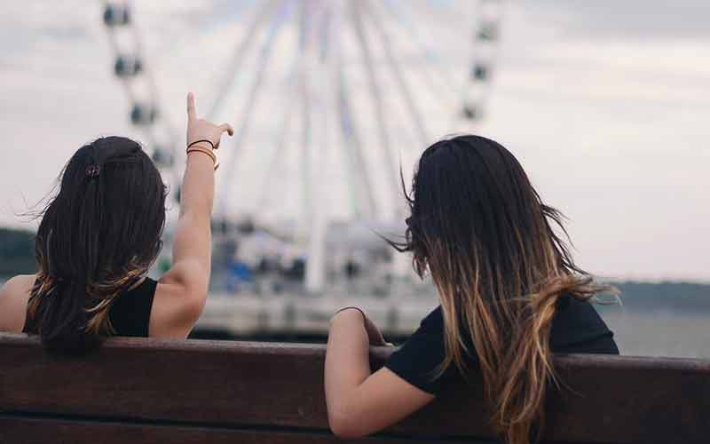 Two women sitting on bench watching ferris wheel