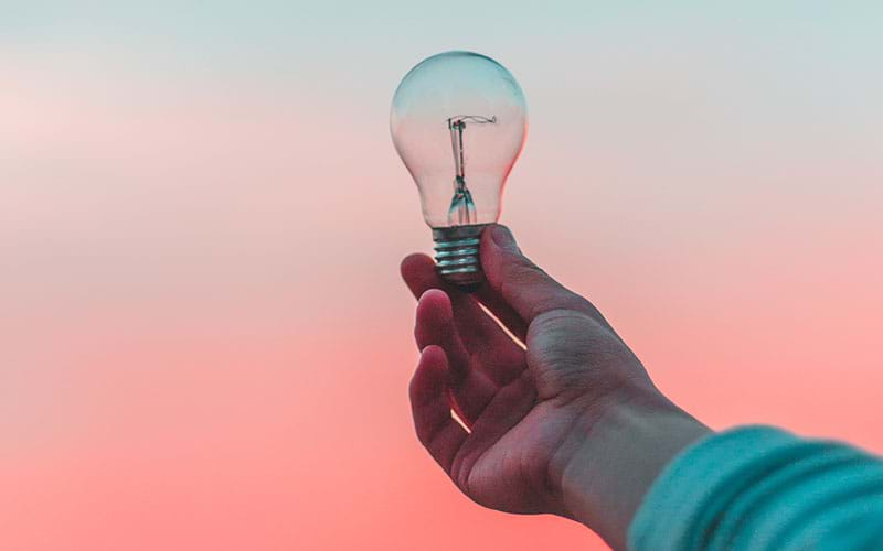 Person holding lightbulb against pink and blue background