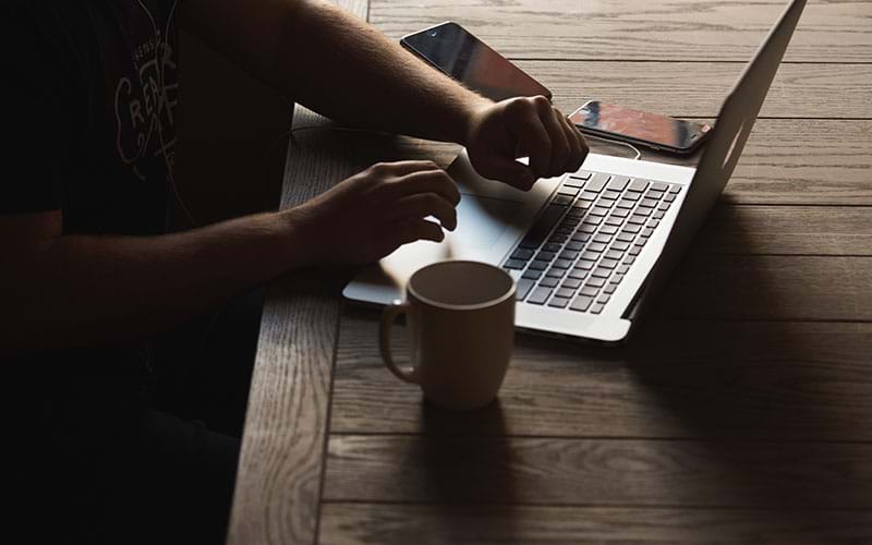 Person working on laptop next to coffee mug