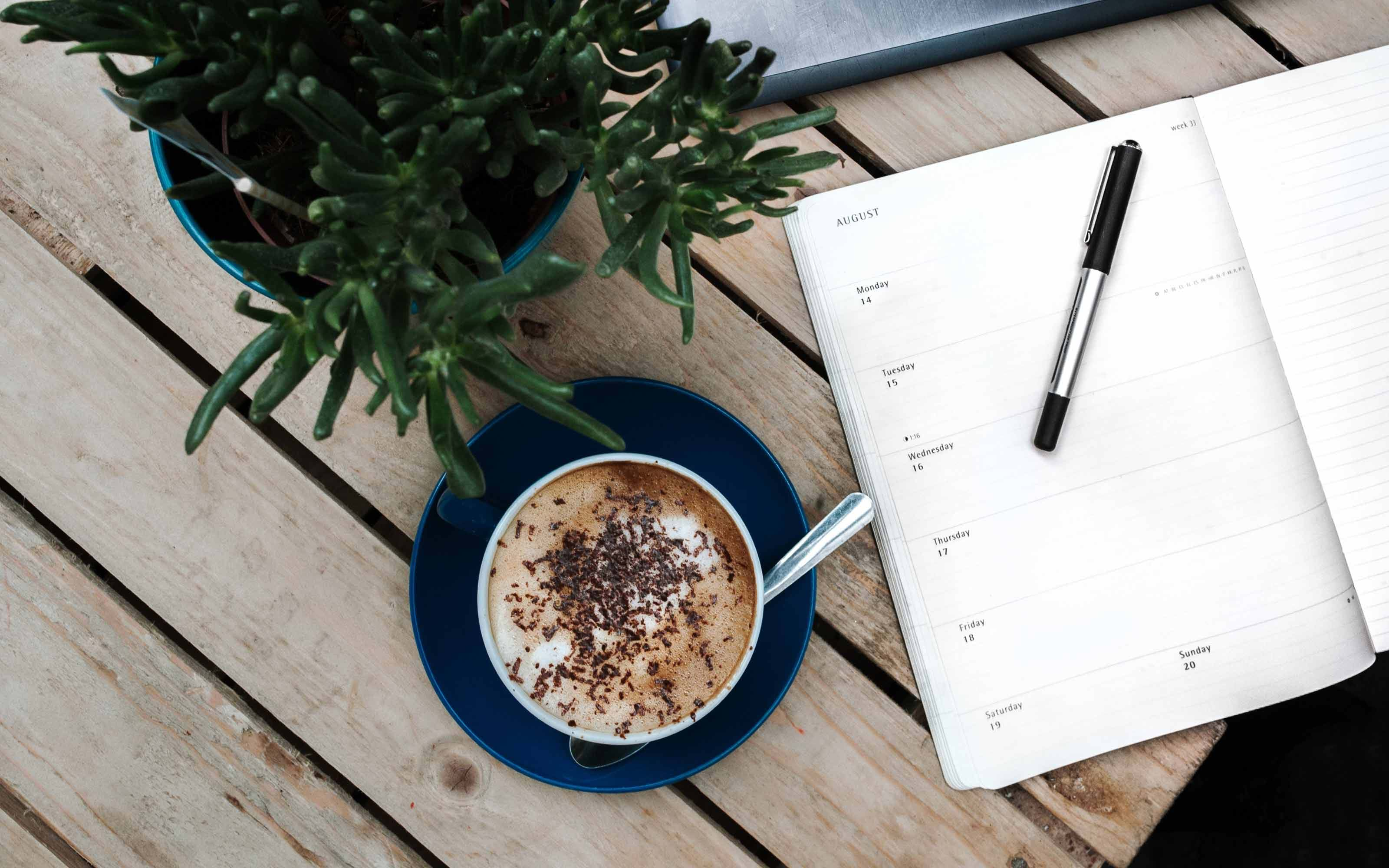 Cup of coffee on table next to open planner