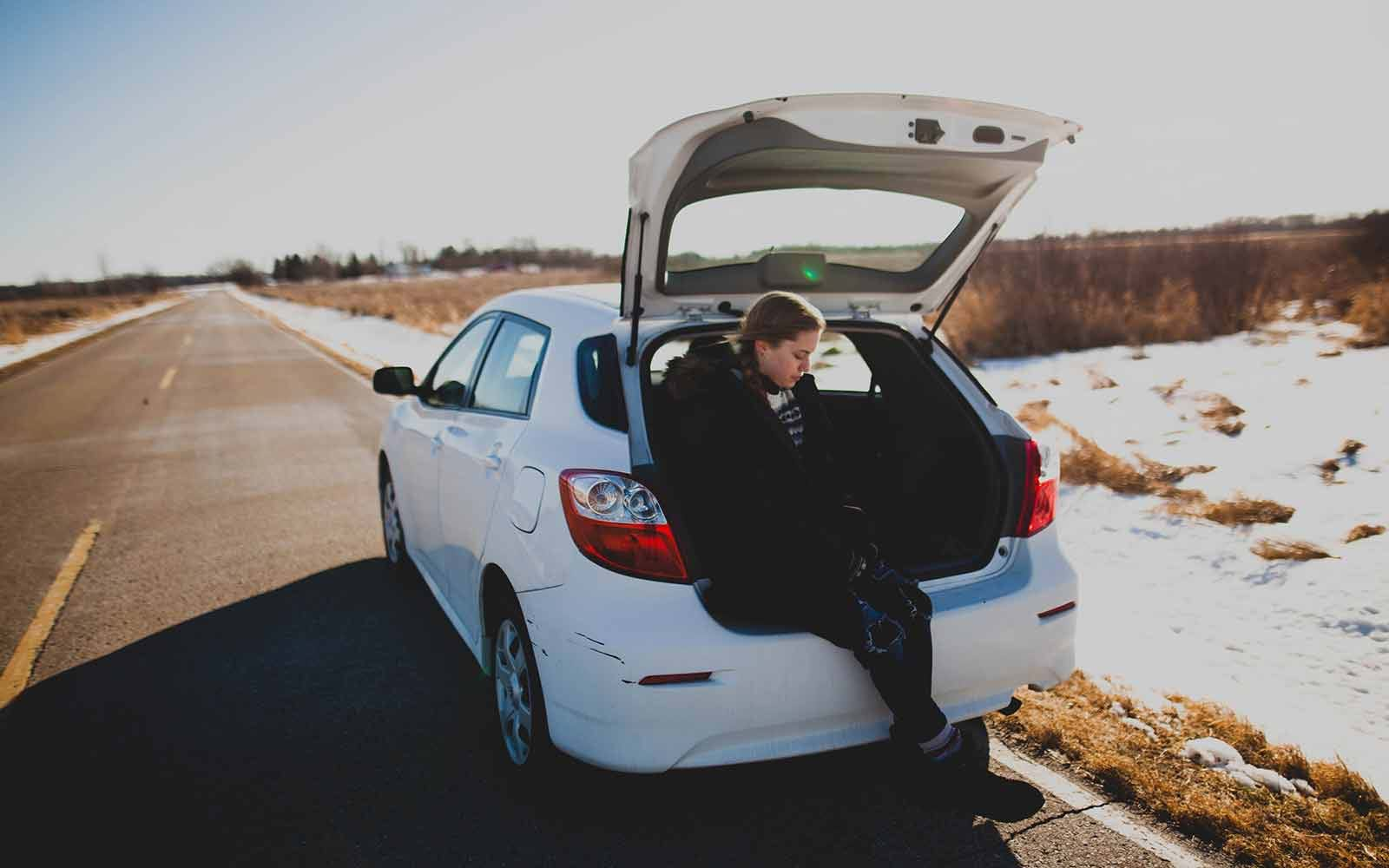 Woman sitting in car trunk on country road