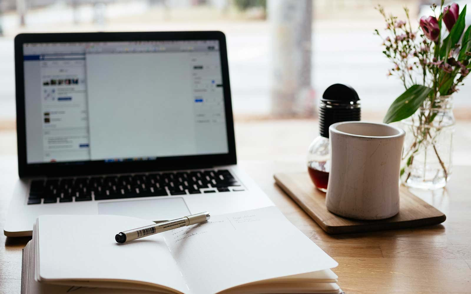 Laptop next to mug and open notebook