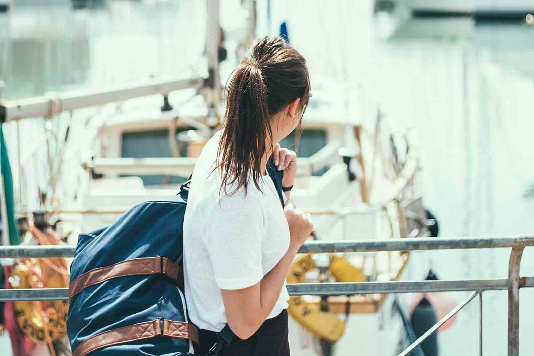 Woman carrying bag past docked sailboat