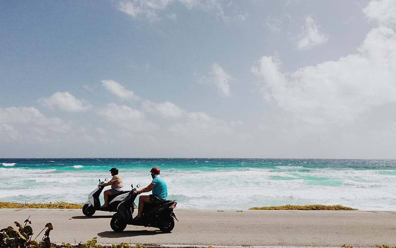 Two people riding mopeds by the ocean