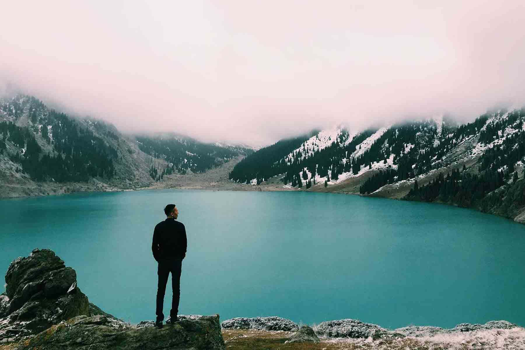 Man on cliff overlooking lake with heavy fog overhead