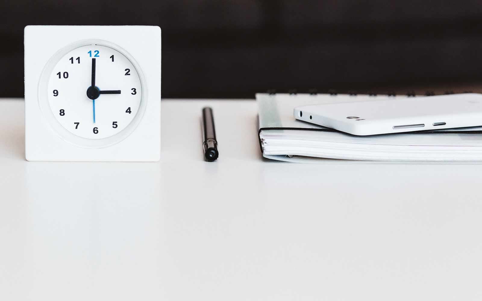 Tiny white clock next to white smartphone and notepad