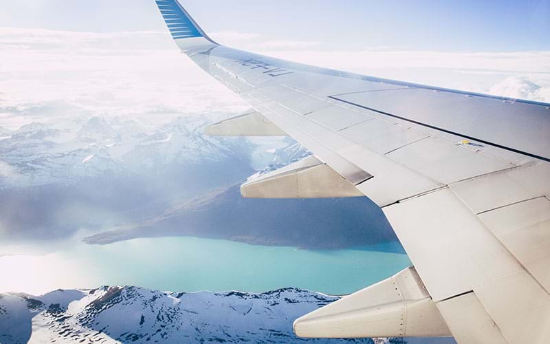 Wing of plane flying over snow covered mountains
