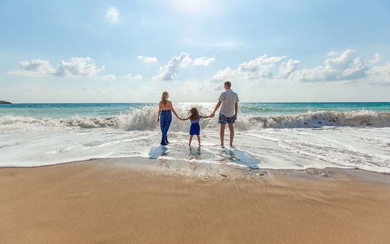 Parents holding hands with child standing in shallow waves