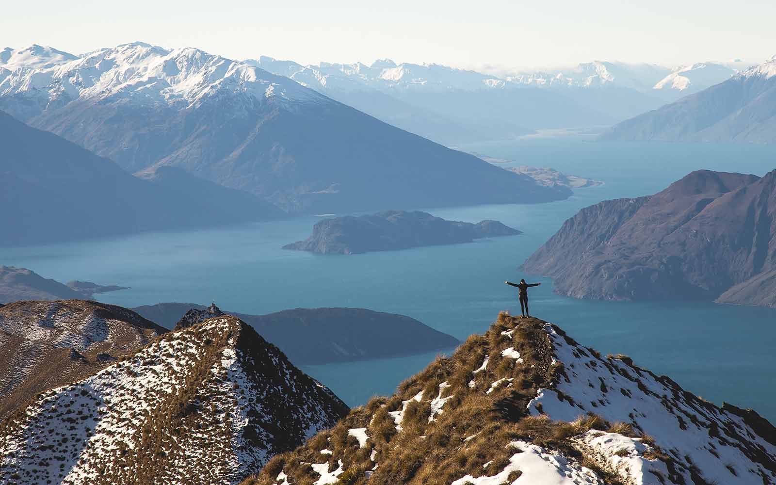 Person standing at peak of a mountain above a river