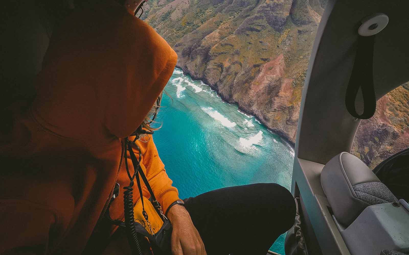 Person riding in helicopter over water and mountain