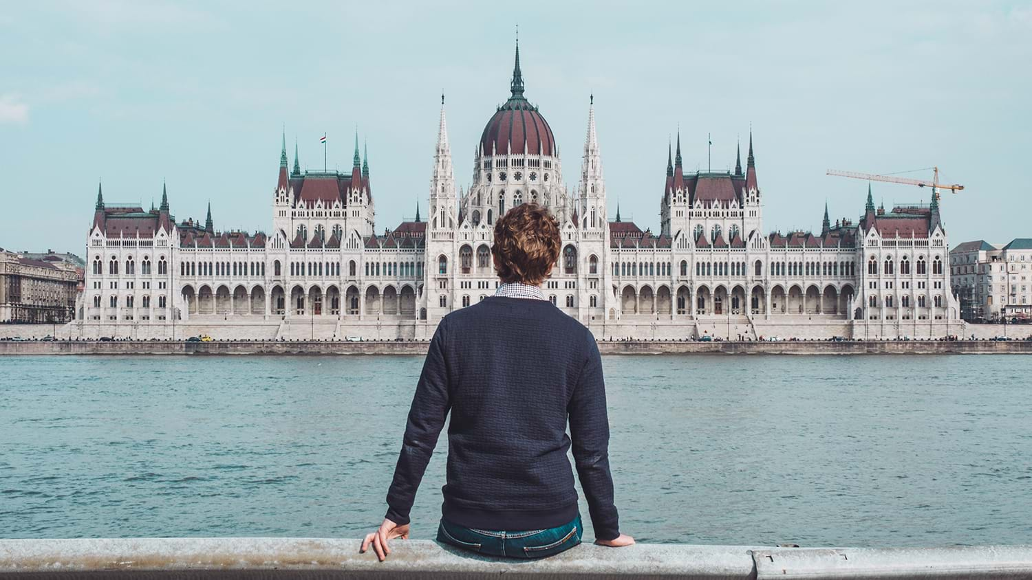 Man sitting and looking across river at parliment building