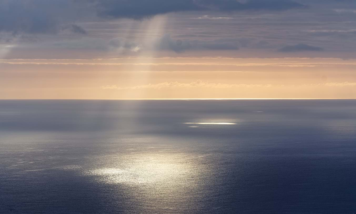 Beams of sunlight shining through clouds onto ocean surface