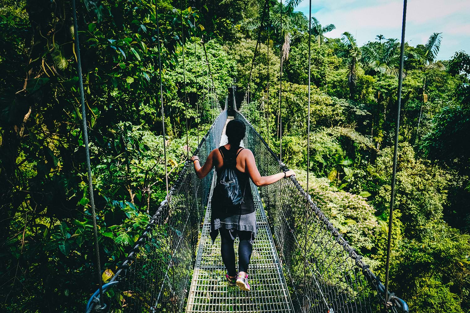 Woman crossing rope bridge over jungle