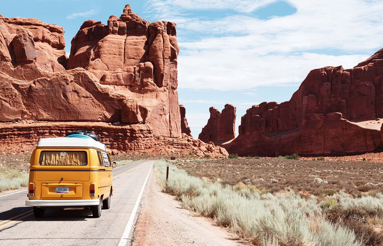 Yellow bus driving through desert toward rock formations