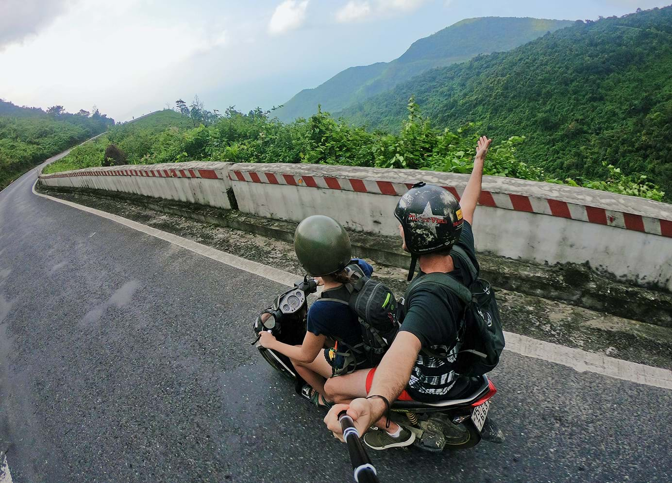 View from selfie stick of two people riding vespa