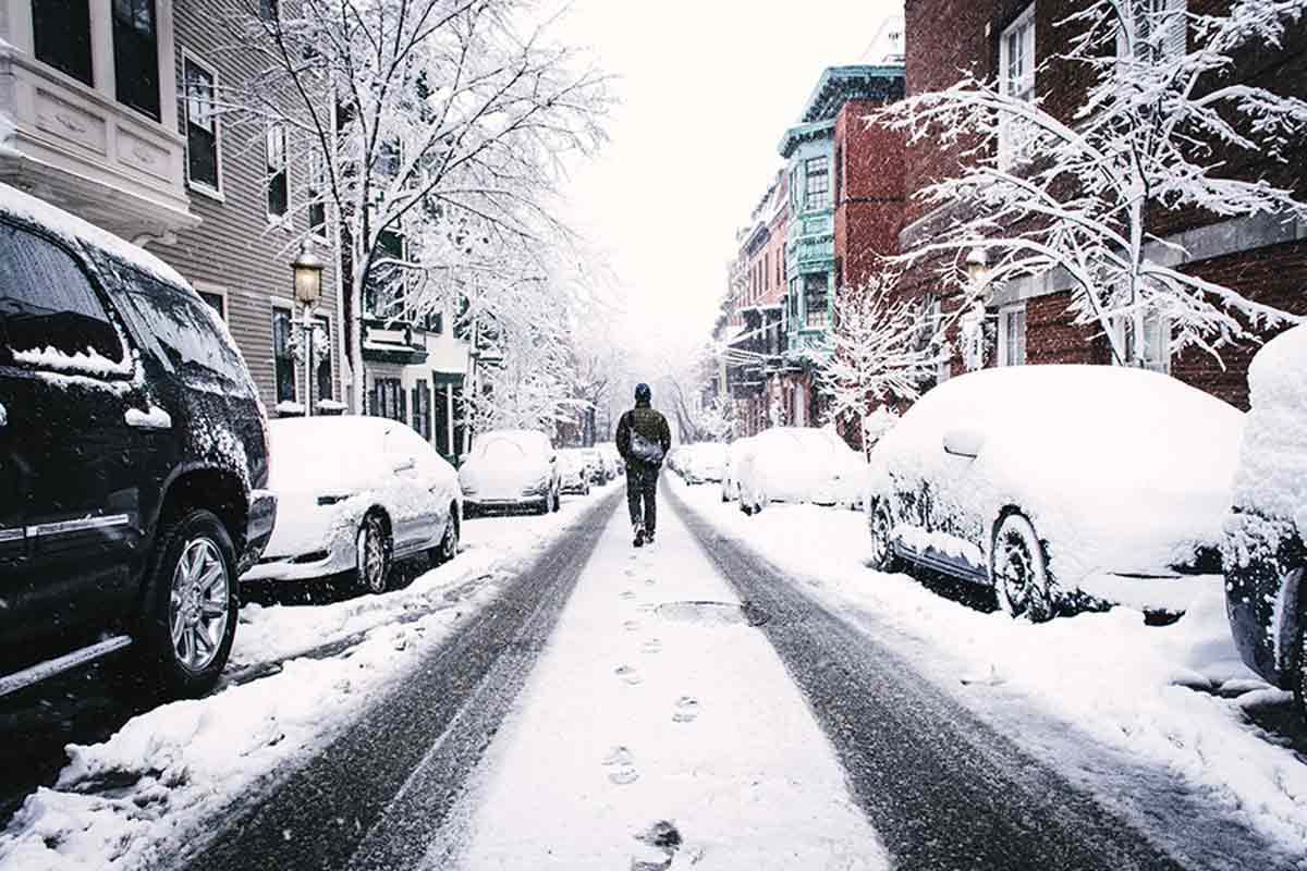Man walking down street with snow covered cars