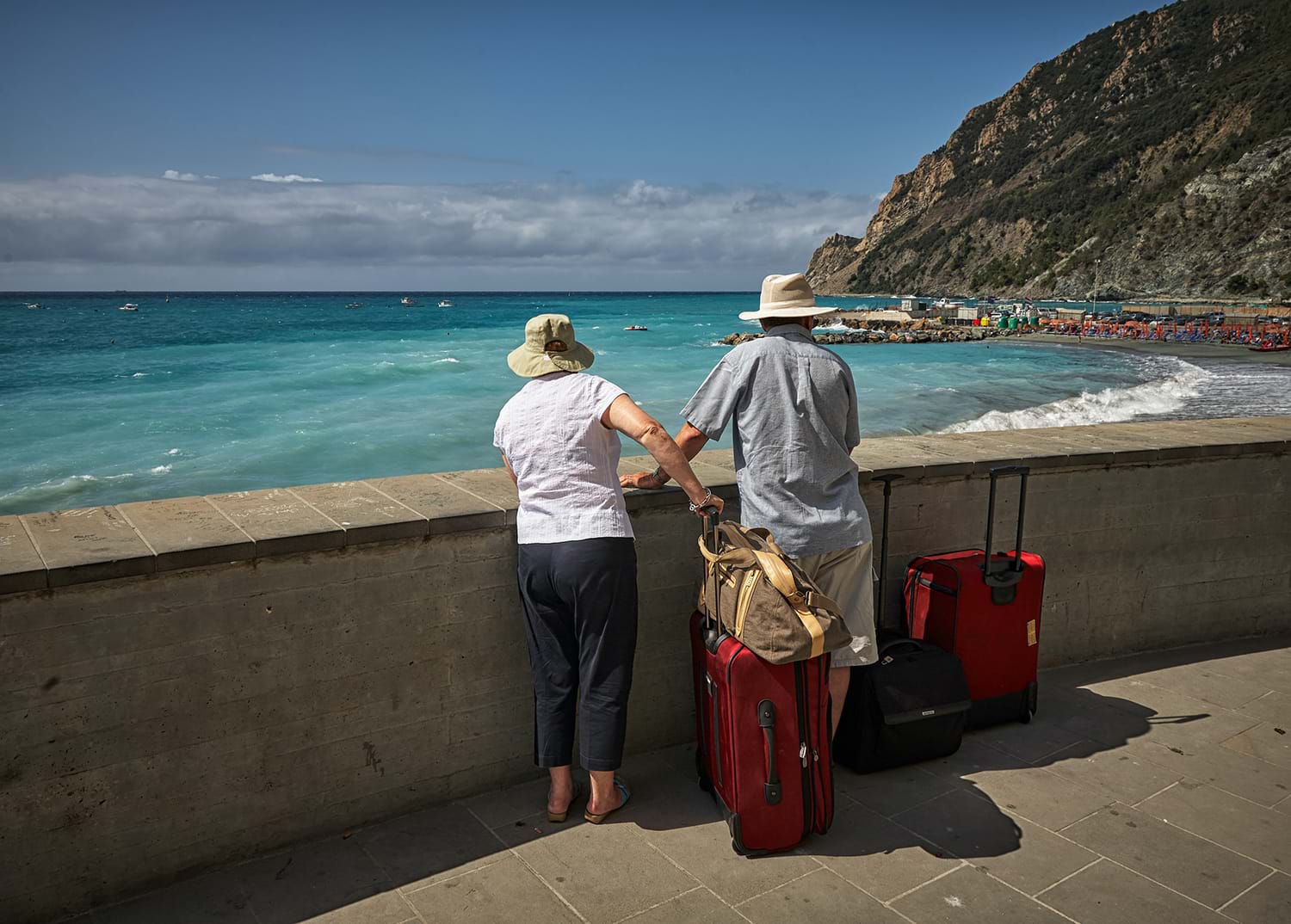 Couple with their luggage standing by wall looking at ocean