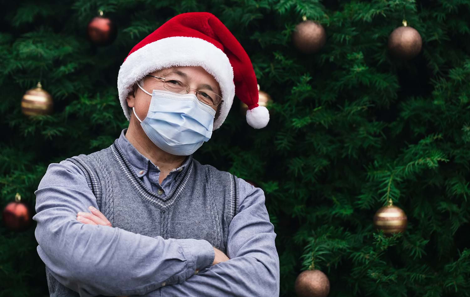 Man in mask and santa hat standing in front of christmas tree