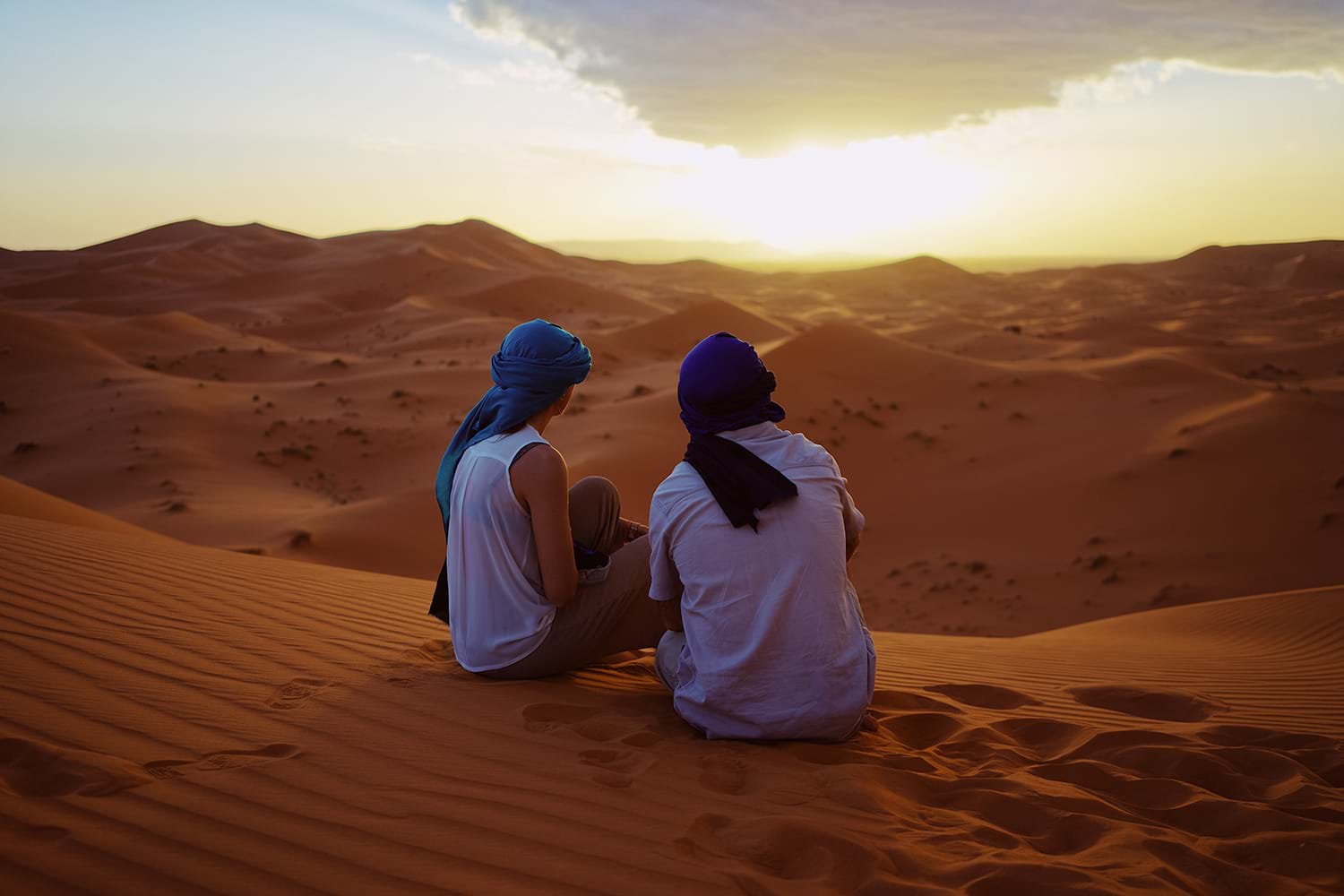 Two people sitting on sand dune in desert