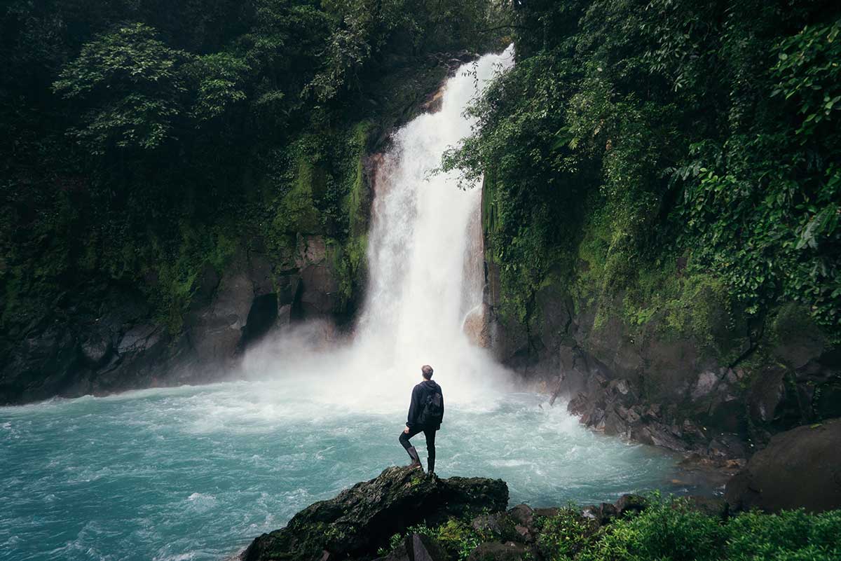 Man standing on cliff watching waterfall