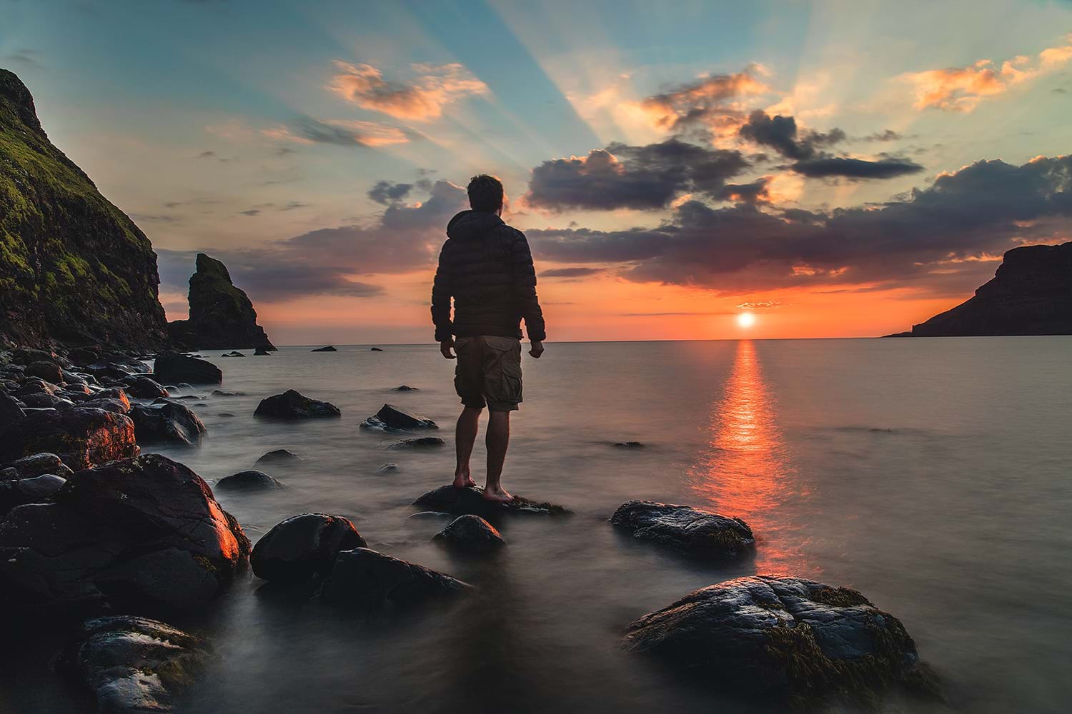 Man standing on rocks in water watching sunset